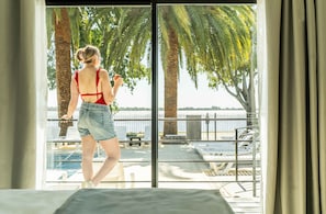 A room with a large sliding glass door leading to a pool area with lounge chairs and palm trees. - Palmas de la Laguna by Posada Suiza (San Miguel del Monte)