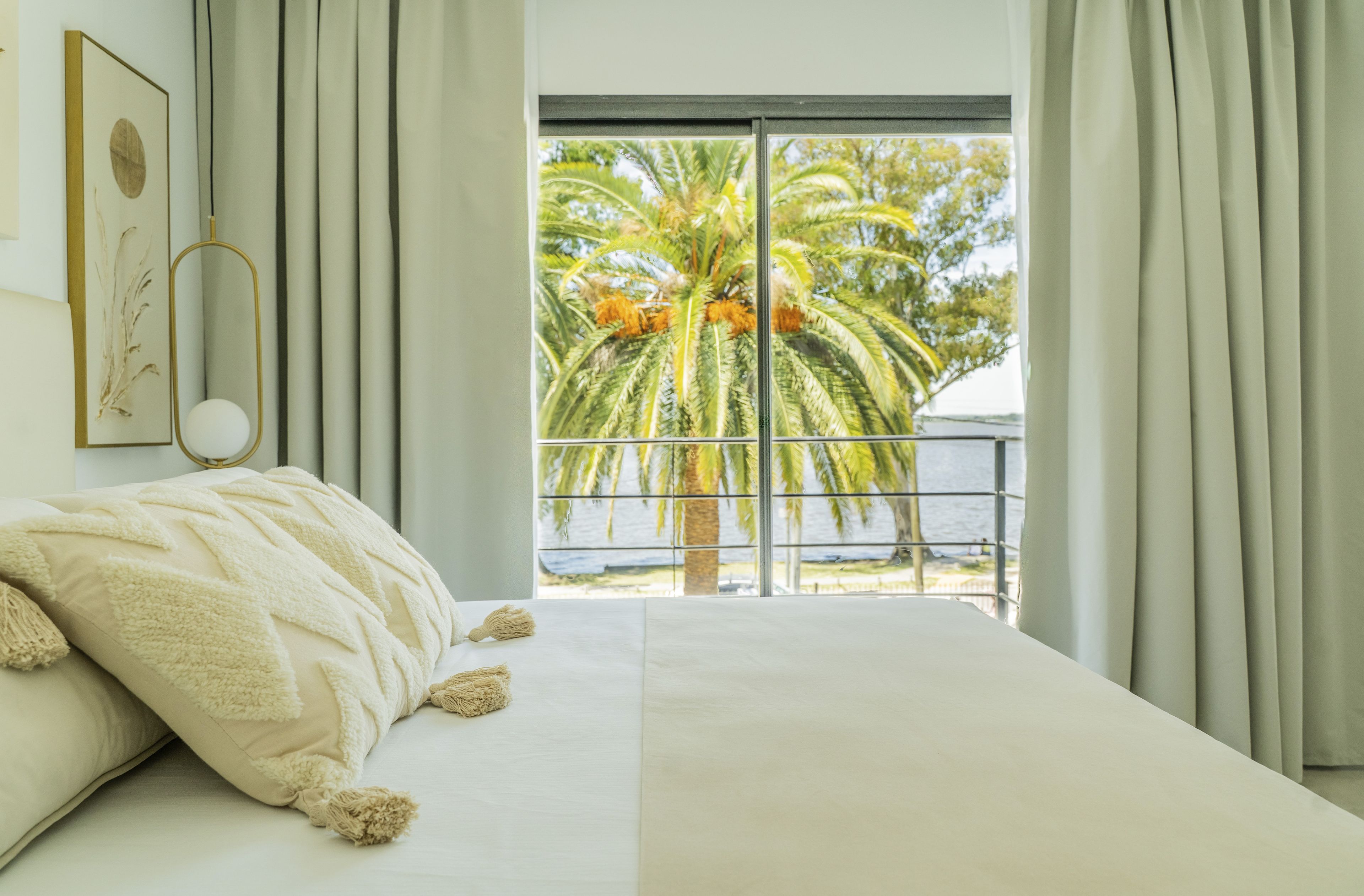A bedroom with a large bed, a view of palm trees, and a balcony.