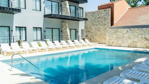 A swimming pool with white lounge chairs, a stone wall, and a modern building with balconies. - Palmas de la Laguna by Posada Suiza (San Miguel del Monte)