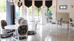 A dining area with white tables and chairs, a chandelier, and a view of the outdoors. - Posada Suiza by Prima Collection (San Miguel del Monte)
