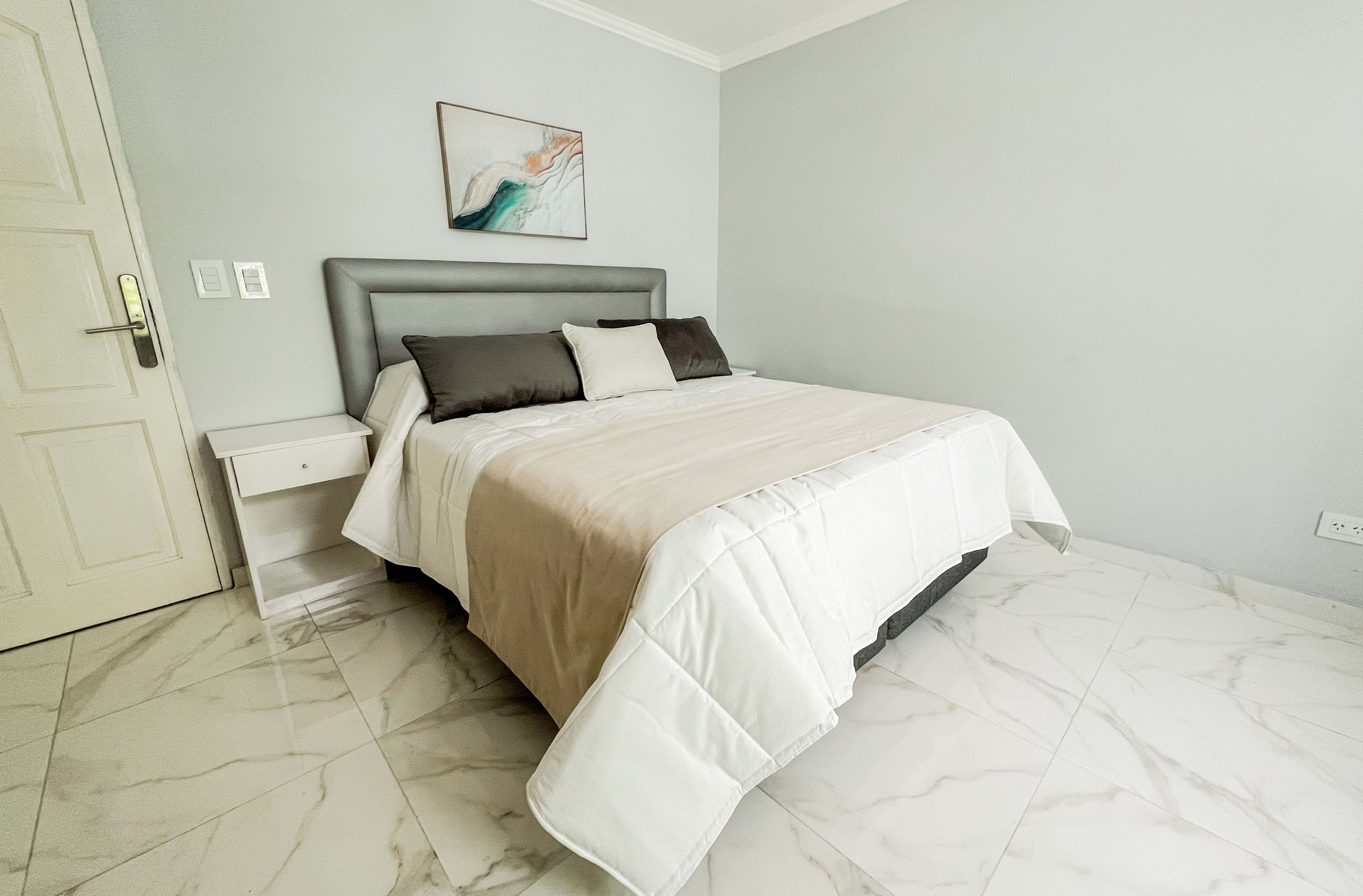 A bedroom with a bed, nightstands, a wall-mounted artwork, and a door.