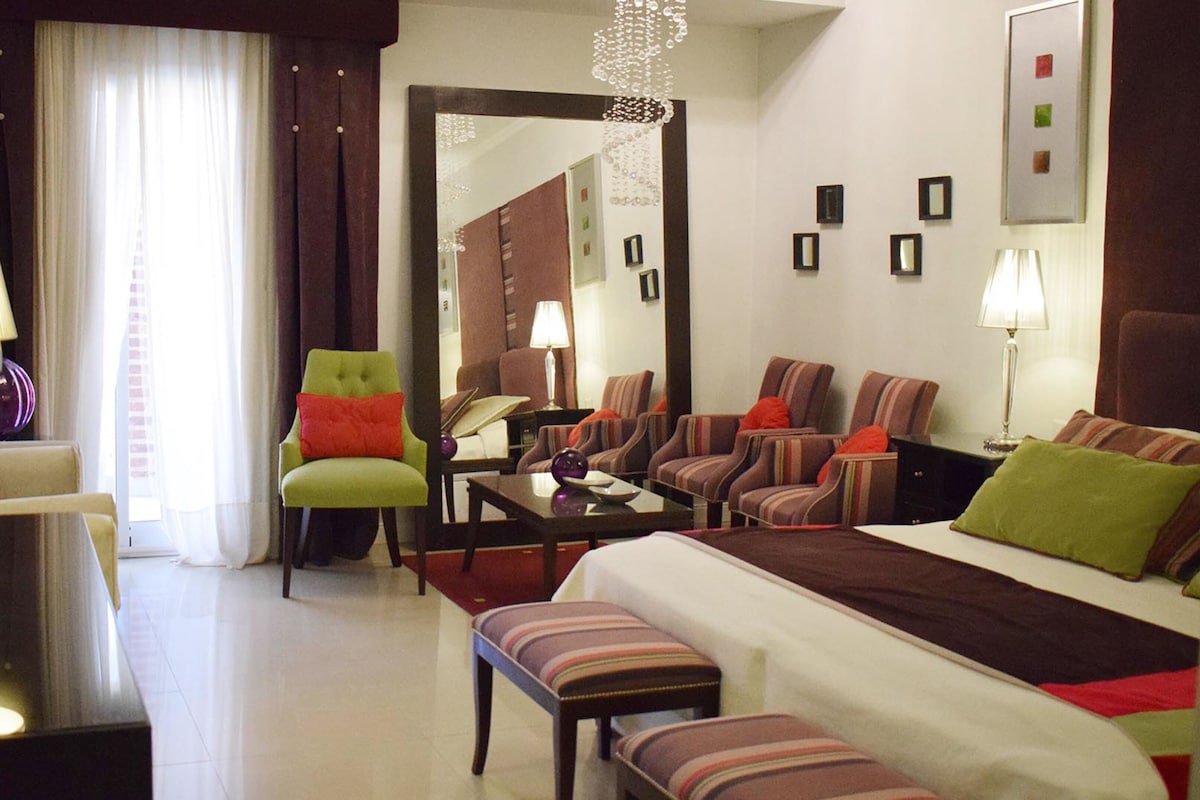 A hotel room with a bed, two armchairs, a sofa, a desk, and a mirror.