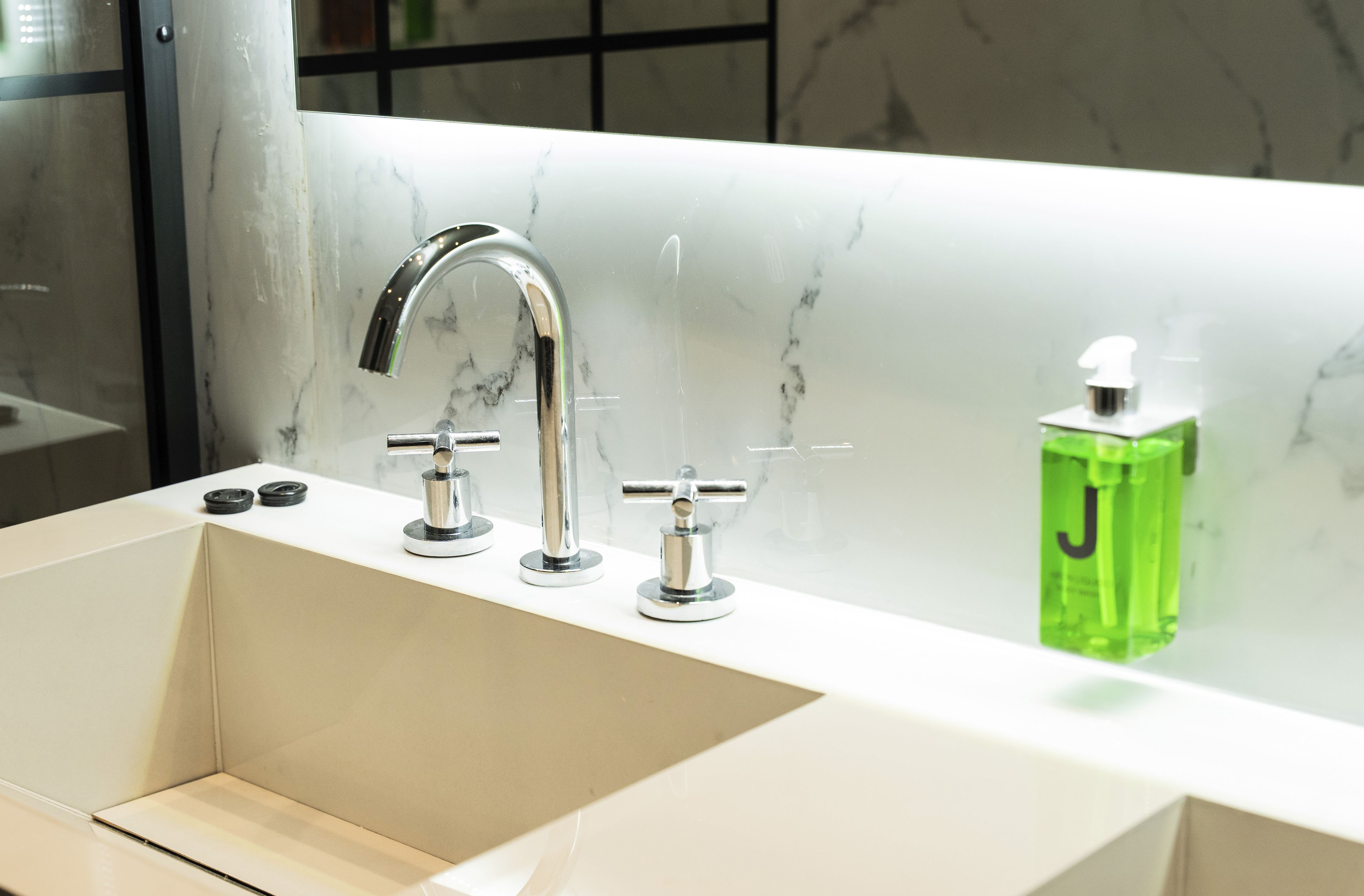 Un baño con un lavabo blanco, grifos cromados y un dispensador de jabón verde.
