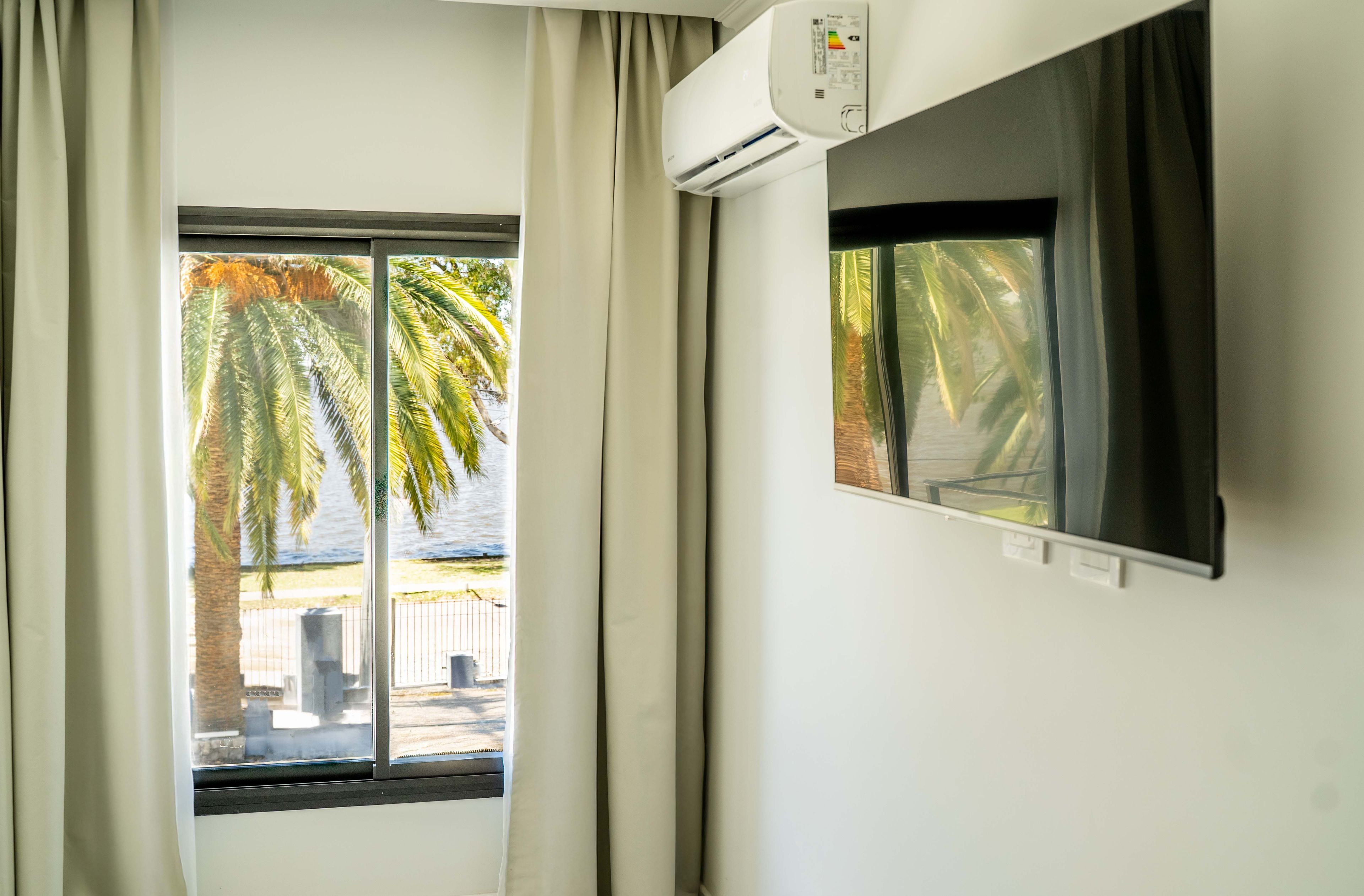 A room with a window, curtains, an air conditioning unit, and a television.