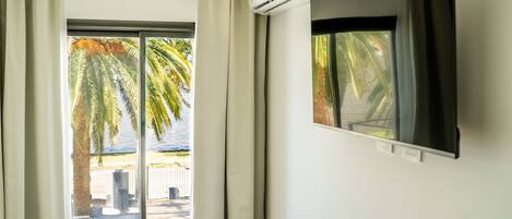 Una habitación con ventana, cortinas, un equipo de aire acondicionado y una televisión.