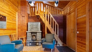 Een gezellig blokhut interieur met een stenen openhaard, twee blauwe fauteuils, een houten trap en een houten deur.