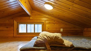 Een kleine, houten slaapkamer op zolder met een enkel bed, een raam en een schuine hemel.