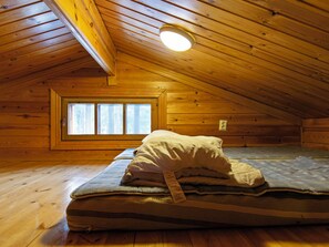 A loft bedroom with a sloped ceiling, a skylight window, and a mattress with pillows.