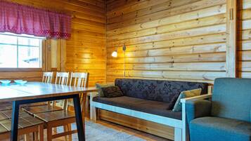 Interior de uma cabana de madeira com uma mesa de jantar, cadeiras, um sofá e um abajur.