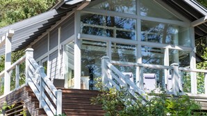 Une cabane moderne dotée d’une grande baie vitrée, d’une terrasse en bois et de rampes blanches.