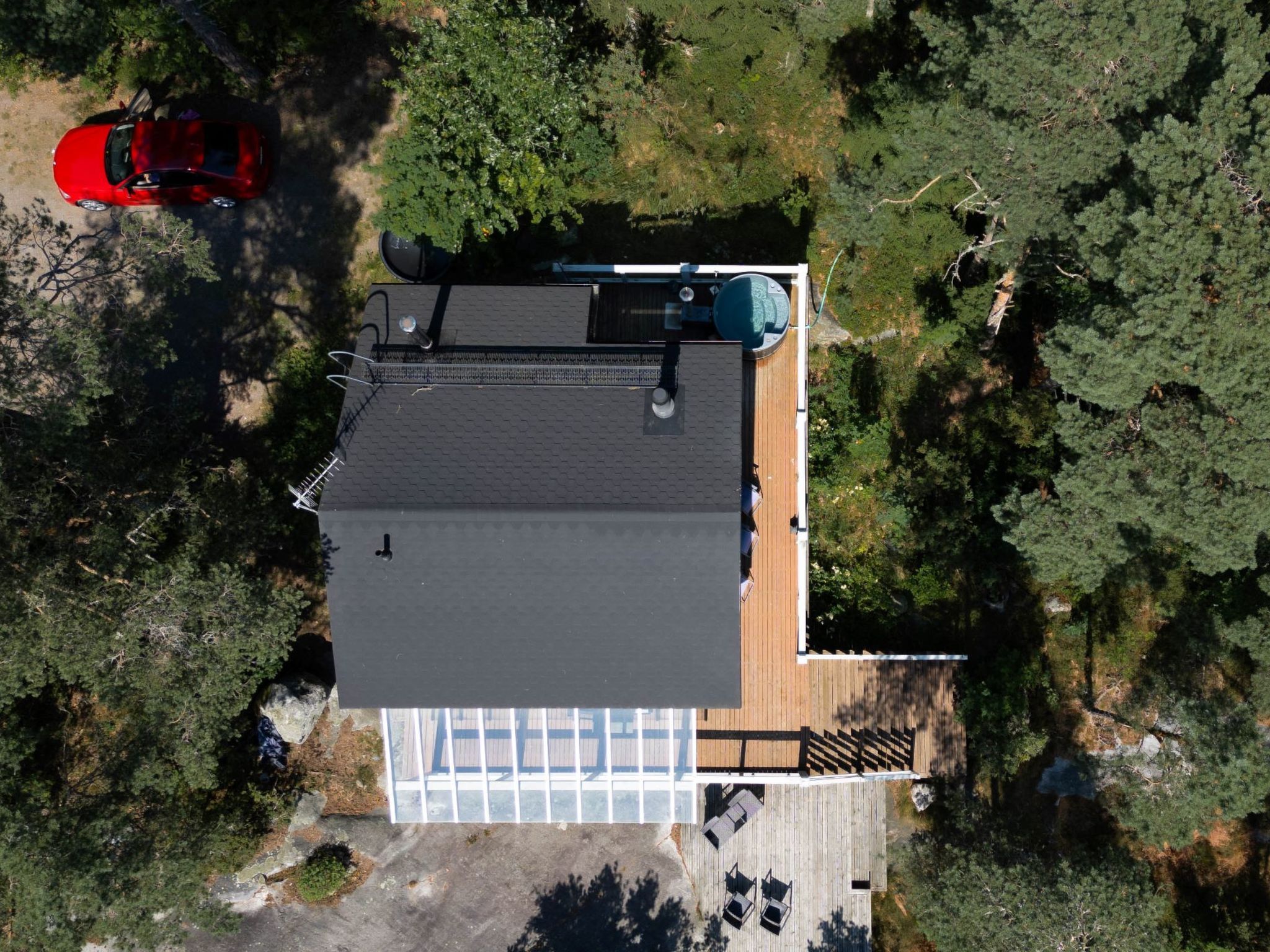 An aerial view of a house with a large deck, surrounded by dense forest.