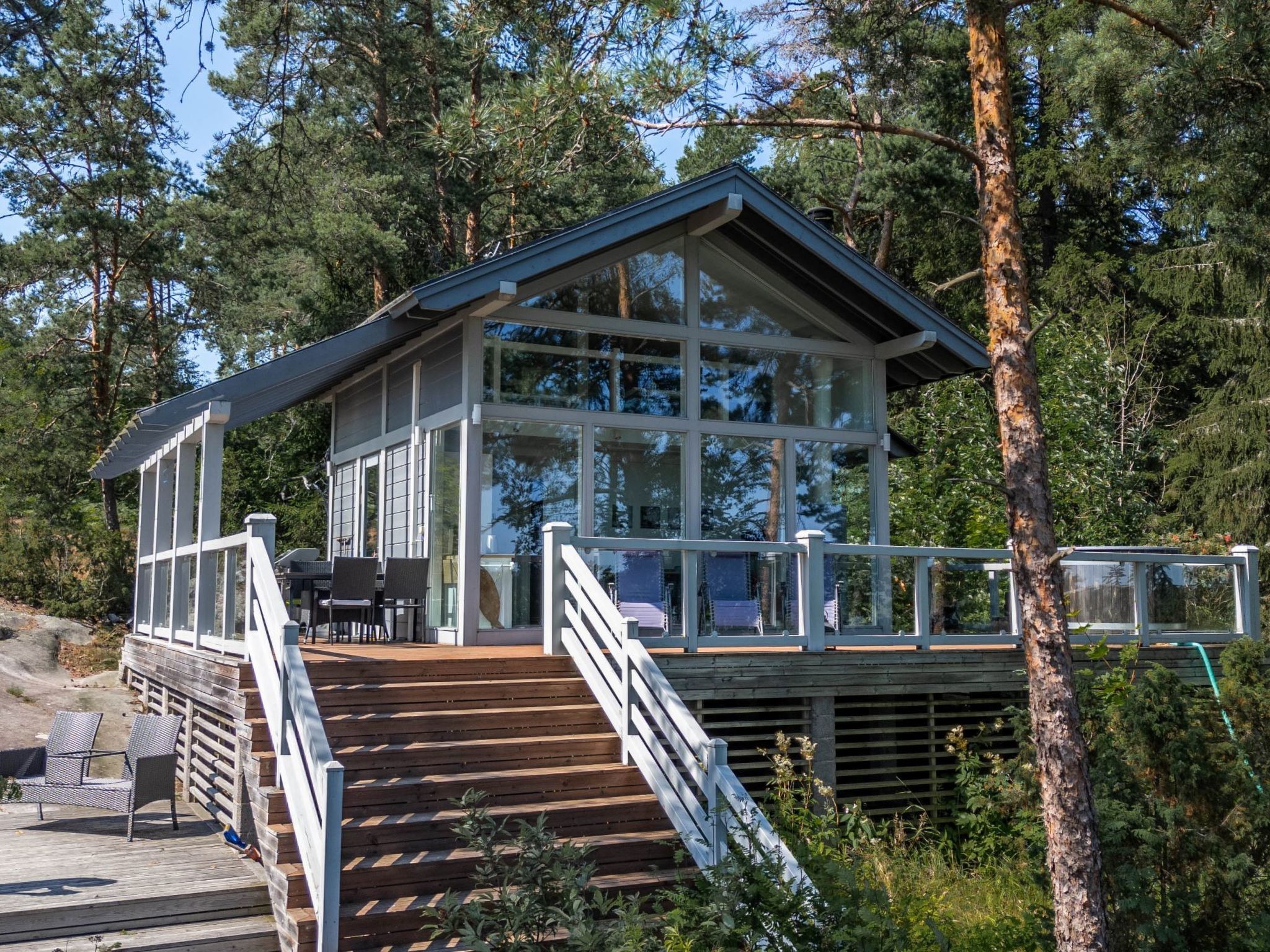 A modern cabin with a wooden deck, glass walls, and a staircase leading to the entrance.