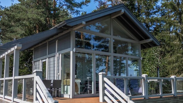 Un bâtiment moderne doté de grandes fenêtres, d’une terrasse en bois et de rampes blanches.