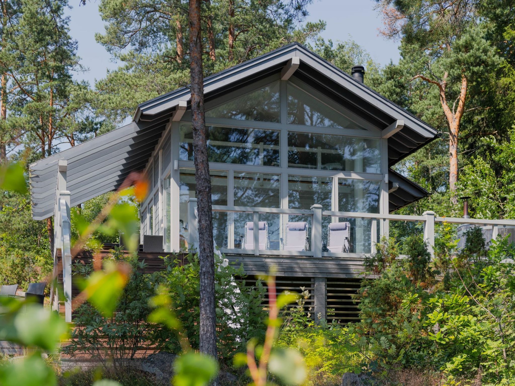 Una casa moderna con ventanas amplias, un balcón y una terraza de madera rodeada de árboles.