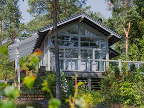A modern house with large windows, a balcony, and a wooden deck surrounded by trees.