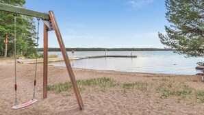Une balançoire en bois installée au bord d’un lac, offrant une vue dégagée sur l’eau et les arbres en arrière-plan.