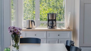 Une cuisine équipée d’une machine à café, d’une bouilloire et d’un vase rempli de fleurs, posé sur le plan de travail.