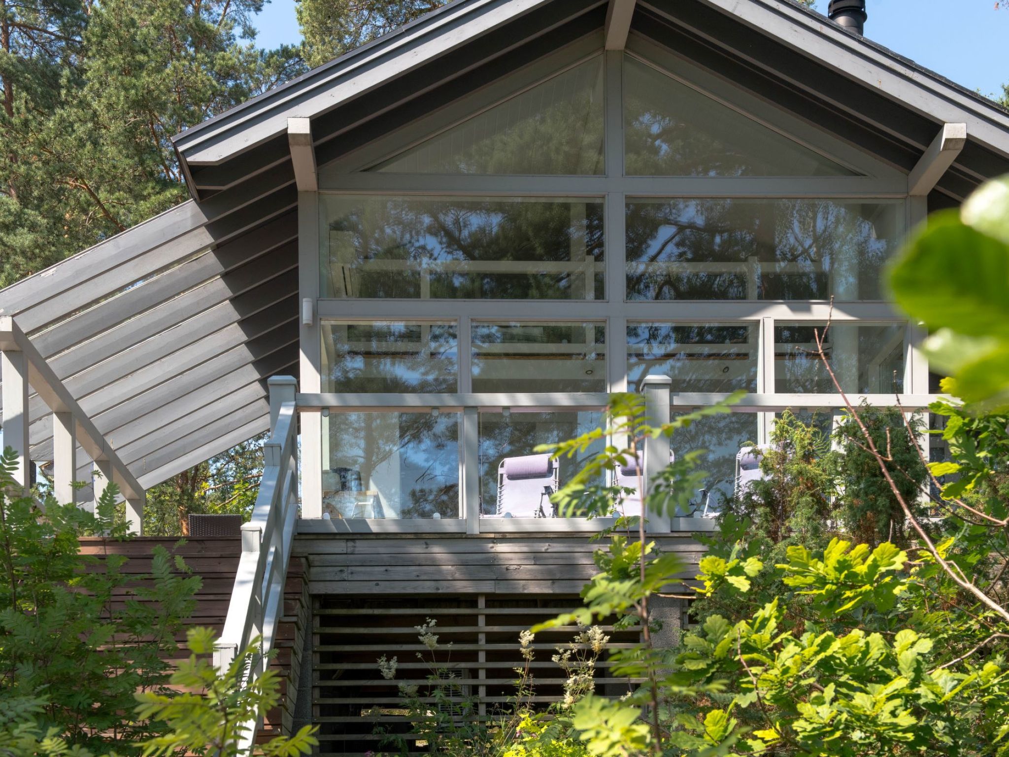 A modern house with a large glass window, a wooden deck, and a metal roof.