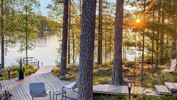 Une terrasse en bois avec des sièges extérieurs et une vue sur un lac entouré d’arbres.