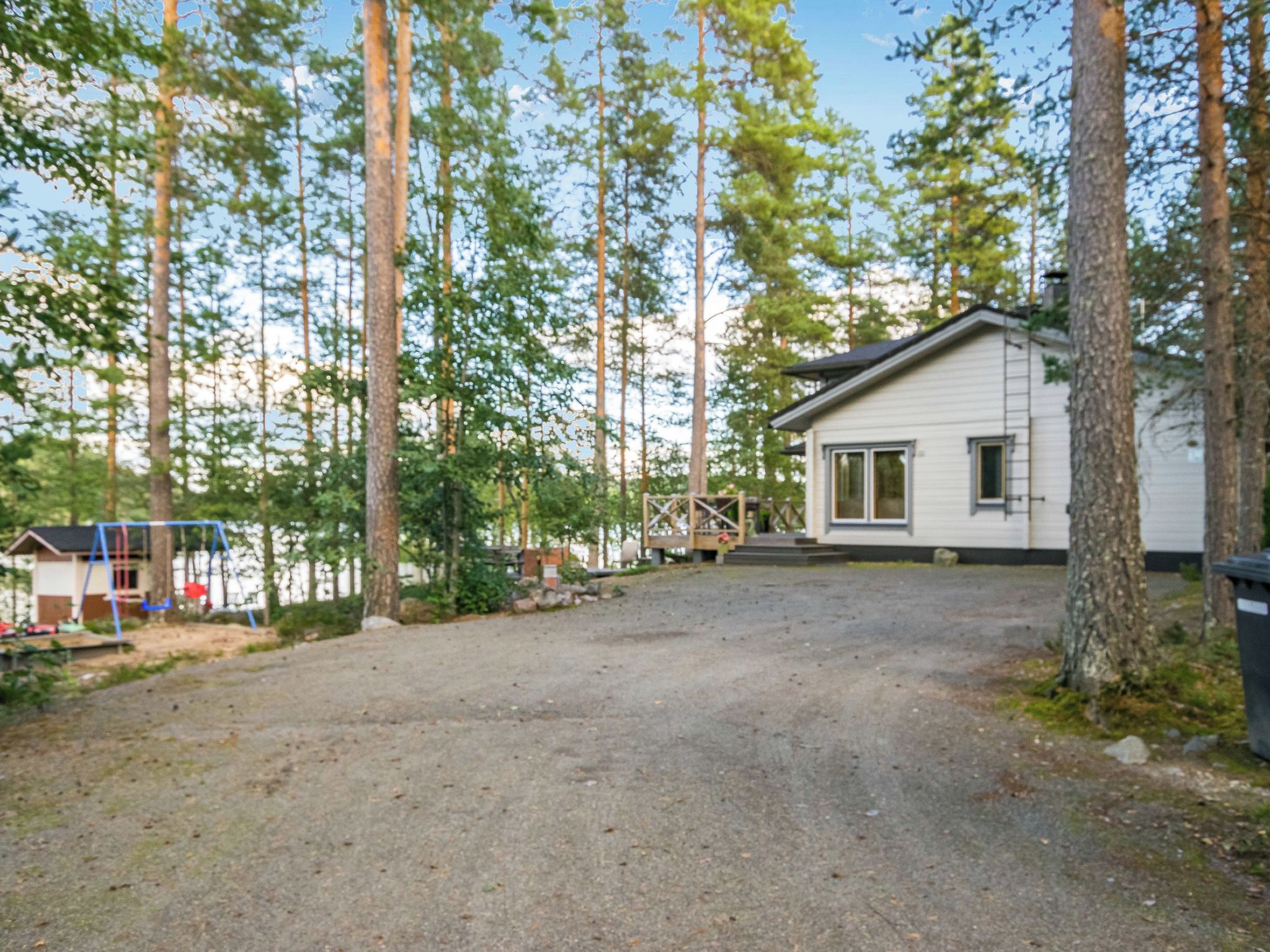 Et etplanshus med grusvej, omgivet af høje træer.
