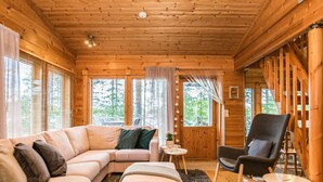 L’intérieur chaleureux d’un chalet comprend un canapé d’angle, un fauteuil, une petite table et un escalier menant à un niveau supérieur.