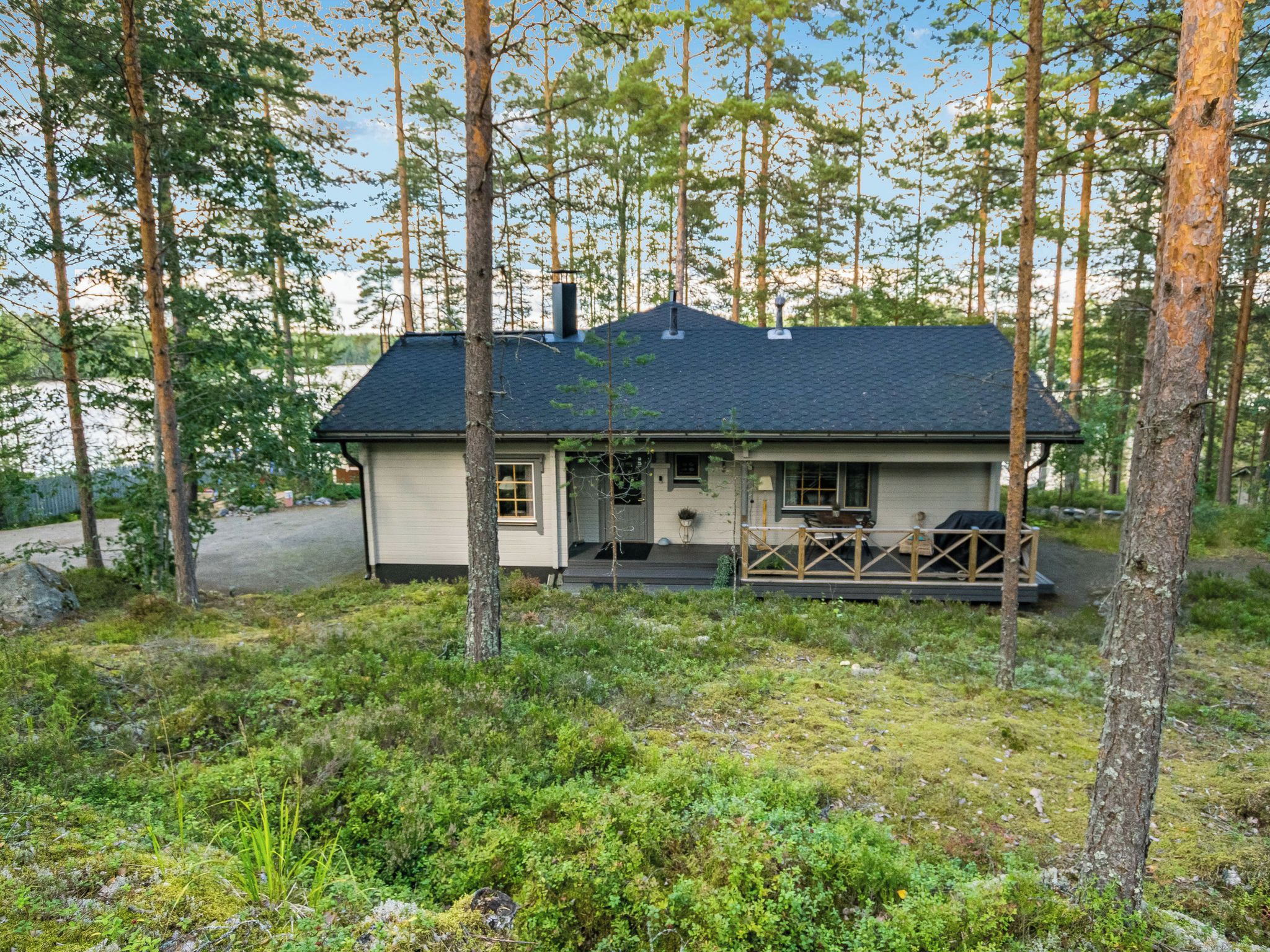 Yhden kerroksen talo, jossa on tumma katto, ja jonka ympärillä on metsäinen alue.