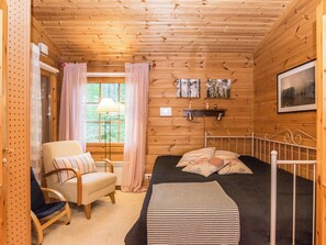 A wooden cabin room with a bed, a chair, a window with curtains, and a wall-mounted shelf with pictures. - Kissankulma by Interhome (Mäntyharju)