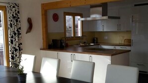 Une cuisine moderne avec des meubles blancs, un plan de travail en bois et un coin repas comprenant une table et des chaises.