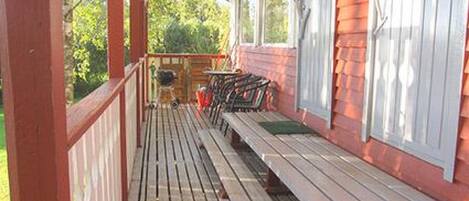 Une véranda avec des bancs en bois et une table, donnant sur un jardin.