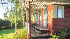 Een rood huis met een veranda, nummer 385, en een gazon.