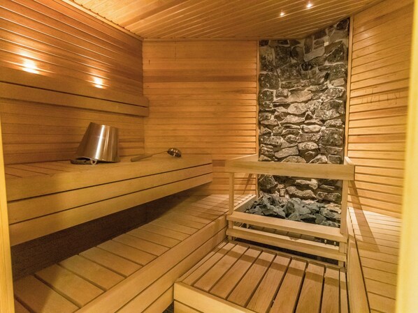 A sauna with wooden benches, a stone wall, and a metal container.
