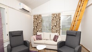 A modern living room with a sofa, two armchairs, a small white table, and a purple rug. There is a wooden ladder against the wall and an air conditioning unit mounted on the wall. - Koivukuja, katinkullantie by Interhome (Sotkamo)