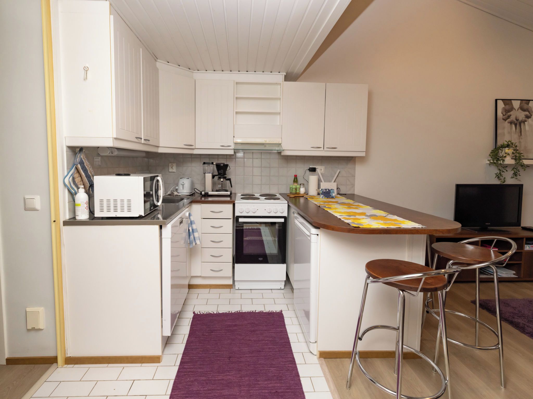 A compact kitchen with white cabinets, a microwave, a stove, and a small bar area with two stools.