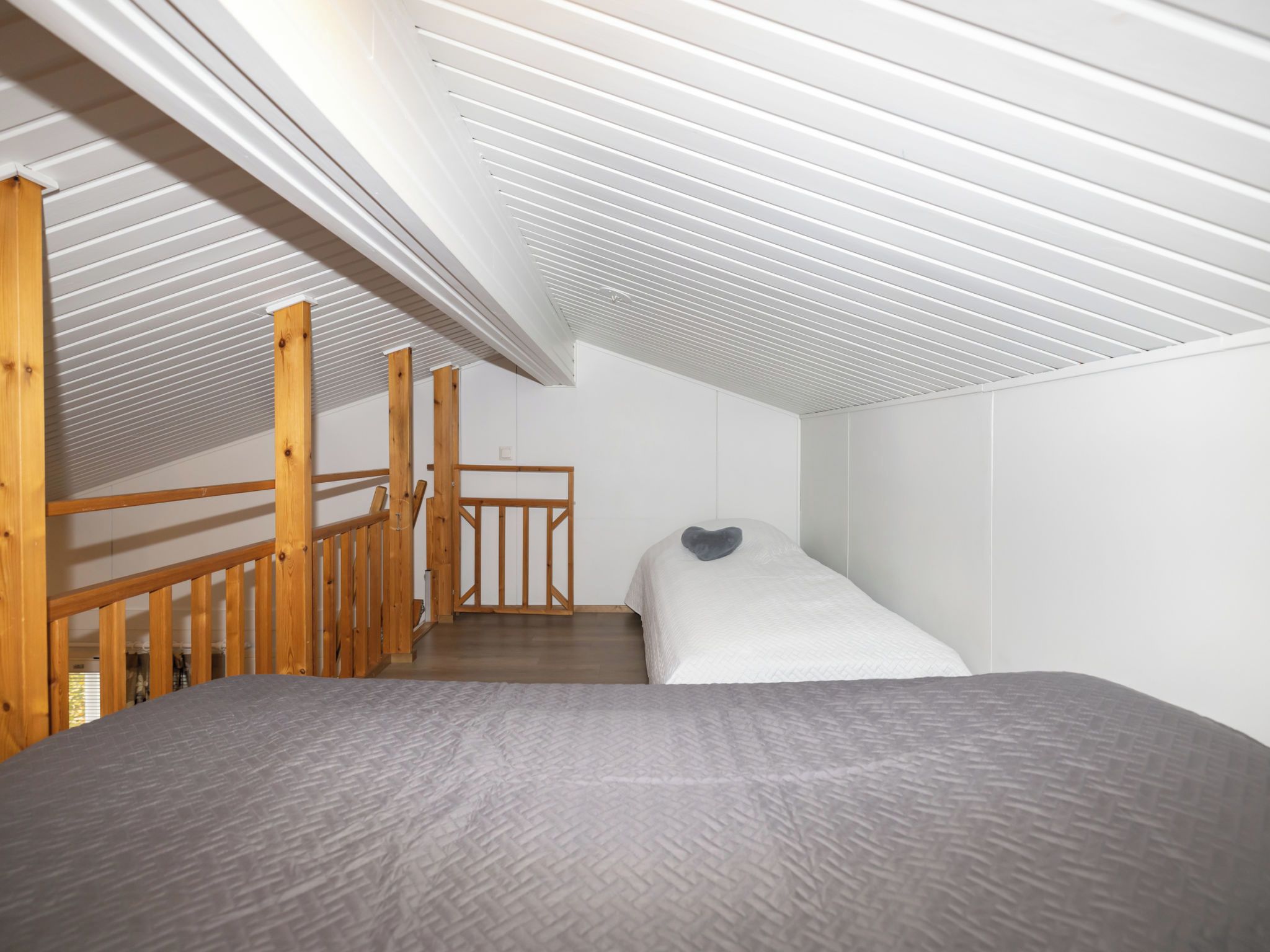 A bedroom with a bunk bed, wooden staircase, and a sloped ceiling.