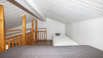 A bedroom with a bunk bed, wooden staircase, and a sloped ceiling.