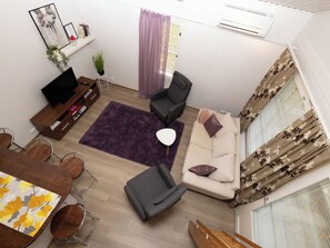 A modern living room with a sofa, chairs, a coffee table, a TV, and a dining area with chairs and a table.