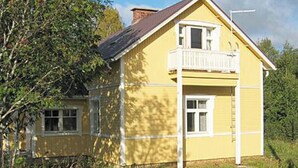 Une maison jaune avec un balcon, entourée de verdure.