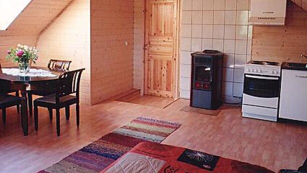 Un intérieur chaleureux et en bois, comprenant un coin repas, une cuisine et une grande fenêtre laissant entrer la lumière naturelle.