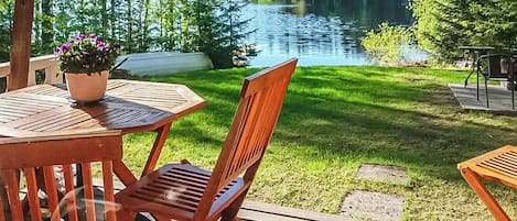 A wooden deck with a table and chairs overlooking a lake surrounded by trees.