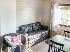 Una habitación con sofá, sillón, mesa y ventana con cortinas.