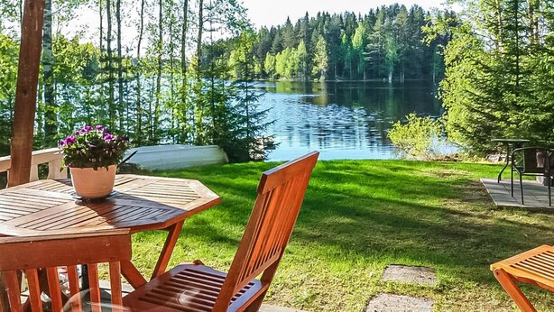 A wooden deck with a table and chairs overlooking a lake surrounded by trees. - Kuusela by Interhome (Kaavi)