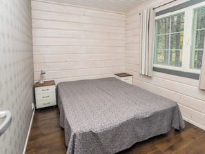 A bedroom with a bed, a nightstand, a window with blinds, and a patterned wall.