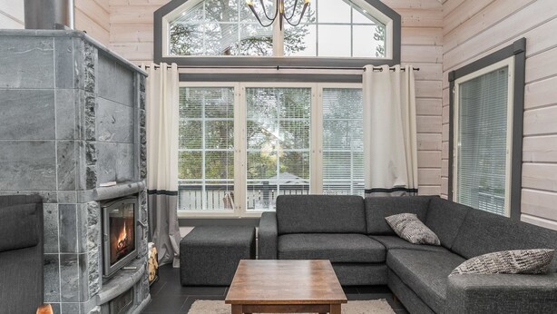 A cozy living room with a stone fireplace, grey sofas, a wooden coffee table, and large windows with blinds. - Rukanloisto b by Interhome (Kuusamo)