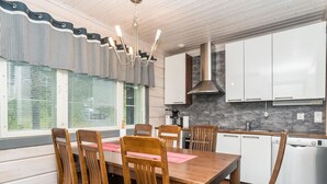 A modern kitchen with white cabinets, a stainless steel range hood, and a large window with blinds. - Rukanloisto b by Interhome (Kuusamo)