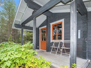 A wooden cabin with a porch, a wooden door, and a window with a lantern.