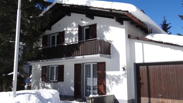 A two-story house with a balcony, a garage, and a snow-covered roof.