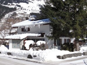 A two-story house with a snow-covered roof and icicles hanging from it.