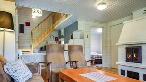 Un salón acogedor con una mesa de madera, dos sillones estampados, un sofá marrón y una chimenea.