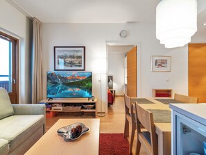 A modern living room with a flat-screen TV, a dining area with wooden furniture, and a red rug.