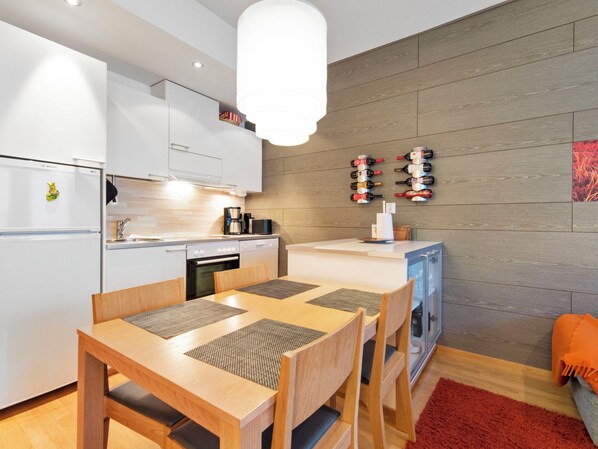 Una cocina moderna con armarios blancos, un refrigerador Bosch, una mesa de comedor de madera con sillas y una estantería para vinos en la pared.